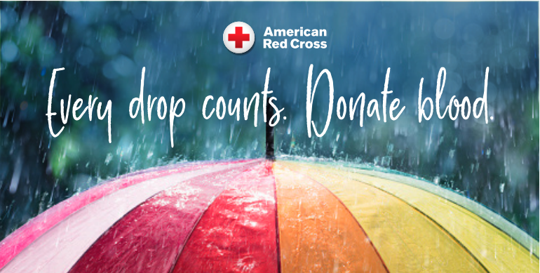A close-up of a colorful umbrella with red, pink, orange, and yellow panels, covered in raindrops. The background is blurred with falling rain. White handwritten-style text reads, 'Every drop counts. Donate blood.' Above the text, the American Red Cross logo is displayed.